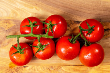 Fresh ripe tomato on a vine in plastic tray on wooden table surface. Organic product. Food supply chain industry. High quality vegetable.