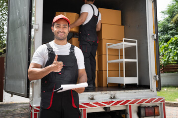 Delivery men use clipboard checking cardboard box with trump up and shipping truck background