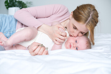 young mother hugging and kissing her baby lying on bed