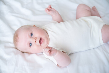 healthy smiling baby lies on his back on bed on white bedding