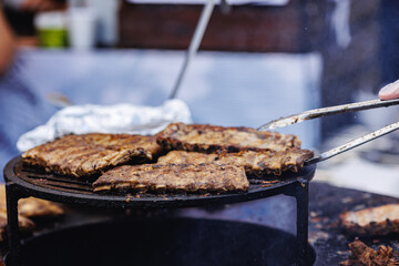 BBQ cook grills pork ribs on open fire. Turns meat over with tongs. Concept Street food