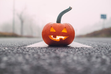 Halloween. A lantern carved from a pumpkin lies on the wet pavement. There is fog behind him. Selective focus.