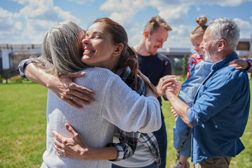 Smiling daughter embracing her senior mother while standing at the green grass lawn