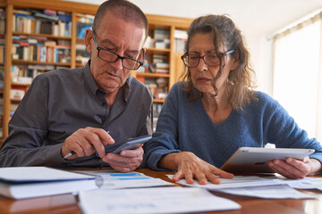 Senior male and senior female  with tablet and calculator anxious while managing bills and paperwork. Couple doing omestic life budget