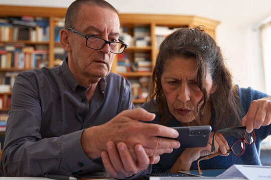 Senior couple shocked looking at smartphone while managing bills. Bank account balance - Powered by Adobe
