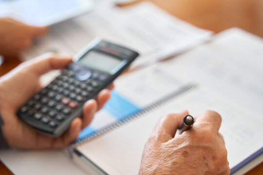 Domestic budget and taxes. Mature male hand writing in notebook by paperwork and bills using calculator