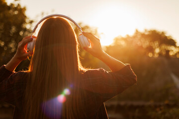 Young woman in headphones listening to music at sunset