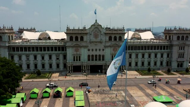 Bandera Guatemalteca ondenado al viento sobre asta en del centro de la capital de la ciudad con palacio nacional de cultura de fondo en Guatemala 