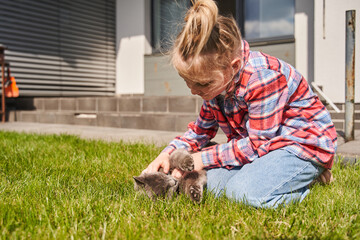 Little cute girl stroking cute grey cat at the green summer lawn