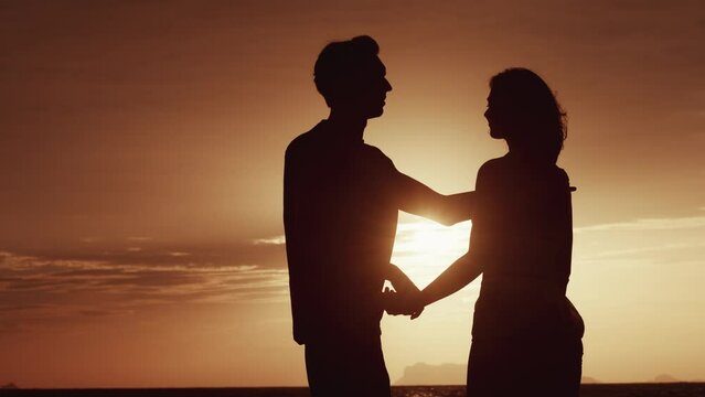 Couple concert. Silhouette of couple in love hold hands in evening on sea sunset. Man shows a dream with his finger to woman on romantic date. Romantic couple dreaming, holding hands at sunset