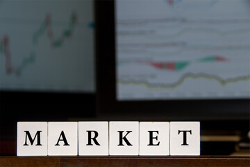 Financial image, the word "market" in front of two computer screens, displaying financial graphs.

