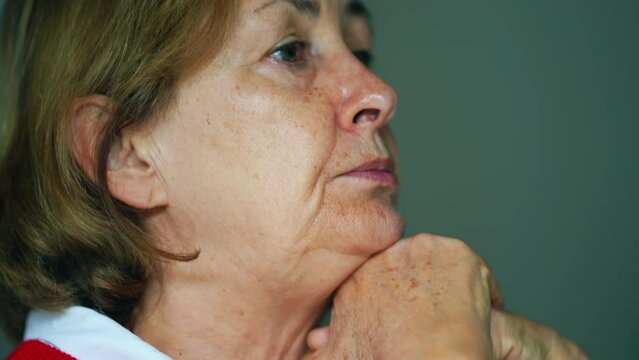 Profile close-up senior woman face with pensive expression and talking in conversation with somebody off-camera. Thoughtful elderly lady pondering solution while speaking, hand in chin