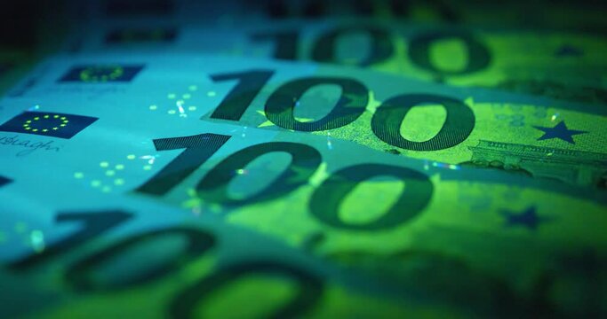 100 Euro banknotes under UV light. Security signs and elements on euro banknotes glow under ultraviolet light