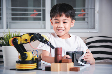 Happy Asian little kid boy using remote control playing robotic machine arm for pick up wood block,...