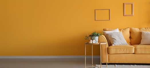 Comfortable sofa with table and houseplants near yellow wall. Banner for design