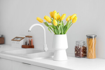 Vase with yellow tulip flowers on countertop near kitchen sink
