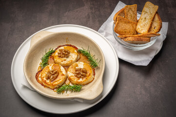 Mediterranean aperitif dish Baked Brie Cheese with Hazelnuts and Honey. With croutons on a dark marble background