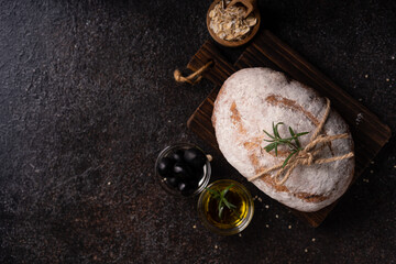 Freshly baked sourdough ciabatta bread with olives and rosemary on a black rustic table. Artisan bread