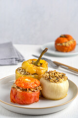 Greek homemade gemista cuisine made of vegetables such as tomato, pepper and onion stuffed with rice and baked until soft served on plate on white wooden table with tableware and towel for dinner