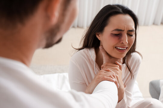 Husband holding his bruised wife by throat in bedroom, closeup. Domestic violence concept
