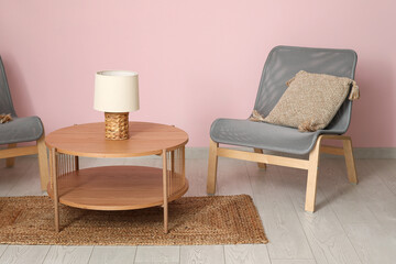 Armchairs with wooden coffee table, lamp and floor mat near pink wall