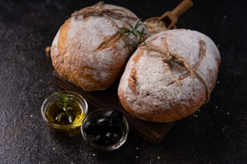 Freshly baked sourdough ciabatta bread with olives and rosemary on a black rustic table. Artisan bread