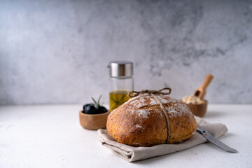 Freshly baked sourdough ciabatta bread with olives and rosemary on a white abstract table. Artisan...