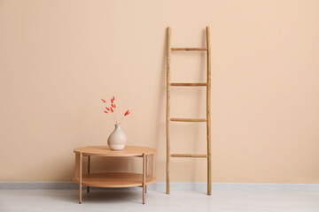 Wooden ladder, table and vase with lagurus near beige wall in room