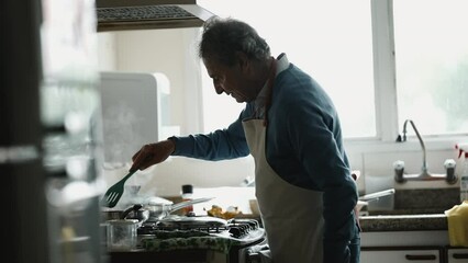 Senior chef cooking food by kitchen stove stirring meal inside pan, Older Man's Detailed food preparation Moment Near sink