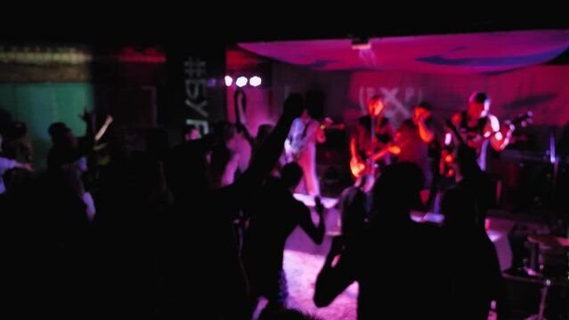 Silhouettes of people partying to music at a rock concert. Blurred video. Open air rock music festival. Light show. Crowd of fans dancing and raising their hands