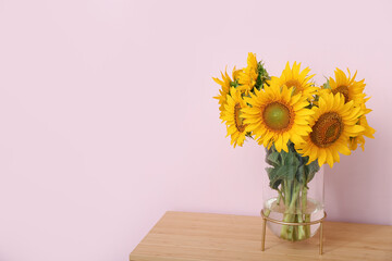 Vase with sunflowers on table near pink wall