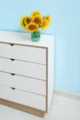 Vase with sunflowers on chest of drawers near blue wall in room
