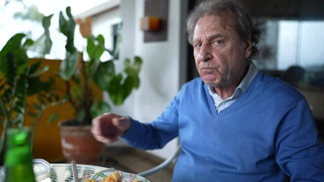 Senior man enjoying pasta food for lunch seated at balcony terrace. elderly retired person in 70s eating during mealtime