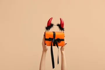 Fotobehang Female hands with Halloween gift box and devil horns on beige background © Pixel-Shot