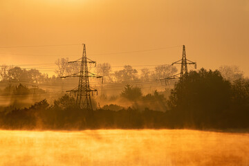 Fog over a river or lake with trees and a high-voltage power line in a summer morning, a landscape in orange color