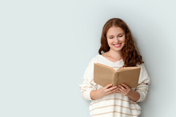 Young woman reading book on light background