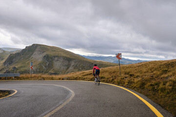 Male cyclist in bikepacking tour.Man cyclist is riding on an empty mountain road with beautiful mountains view.Man cyclist wearing cycling kit and helmet.Gravel bike with cycling bag.Transalpina road.