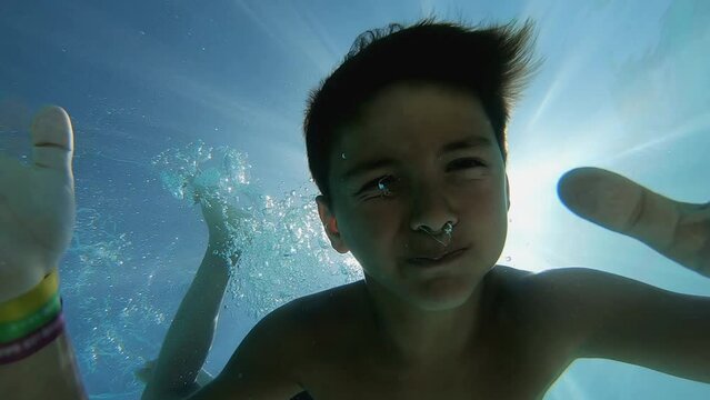 Boy diving deep underwater smiling at the camera and waving