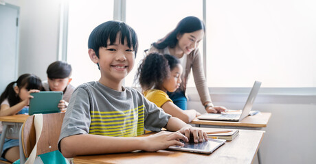 Pupil boy, teacher learn computer in classroom at elementary school. Student boy studying primary school. Children coding online in classroom. Education knowledge, successful teamwork concept banner - obrazy, fototapety, plakaty