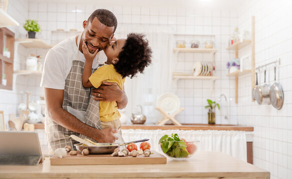 Portrait of little American African black boy parent cooking preparing food with pan in the counter kitchen. Happy  family with father son, father's day, healthcare cooking plant based food concept