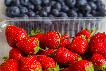 Fresh juicy blueberries and strawberries in a transparent plastic container on the table