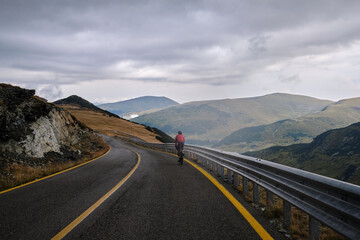 Male cyclist is riding through foggy mountain landscape. Cyclist on a mountain road. Bikepacking on Transalpina road, Romania. Bikepacking journey in Transylvania. Parâng Mountains in the Carpathians.