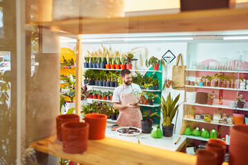 view from the outside of a shop of happy employee gardener working transplanting plants in plant store