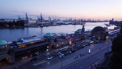 Fototapeta na wymiar Amazing drone point of view in blue hour on Landungsbrucken (station and as terminal for tourboats). In ditance cranes