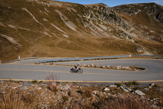Professional female cyclist, dressed in cycling kit and helmet, is training on a gravel bike in the mountains,enjoying an amazing view. Woman cyclist is riding downhill on the Transalpina road.Romania