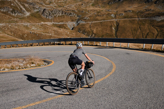 Professional female cyclist, dressed in cycling kit and helmet, is training on a gravel bike in the mountains,enjoying an amazing view. Woman cyclist is riding downhill on the Transalpina road.Romania