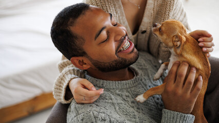 Banner image of smiling african american man in sweater holding chihuahua dog near girlfriend at home