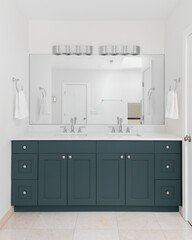 A bathroom with a blue green vanity cabinet, white marble countertop, and stone tile floor.