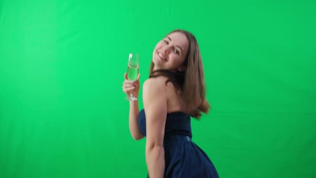 Portrait of smiling confident young woman dancing turning at green screen background drinking champagne. Happy carefree Caucasian lady in elegant dress having fun celebrating at chromakey posing