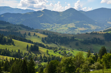 Mountain rural landscape with beautiful village on the hills covered grass and trees. Carpathian Mountains, Ukraine